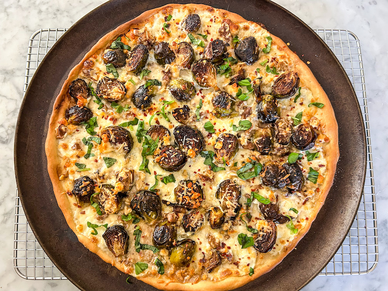 Pizza with sprouts, cheese, walnuts, chili flakes, and herbs, cooling on a wire rack