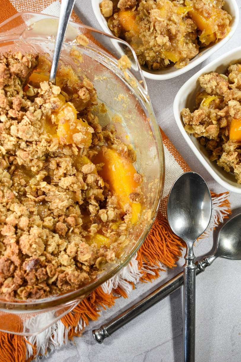 A glass baking dish of peach crisp and two spoons