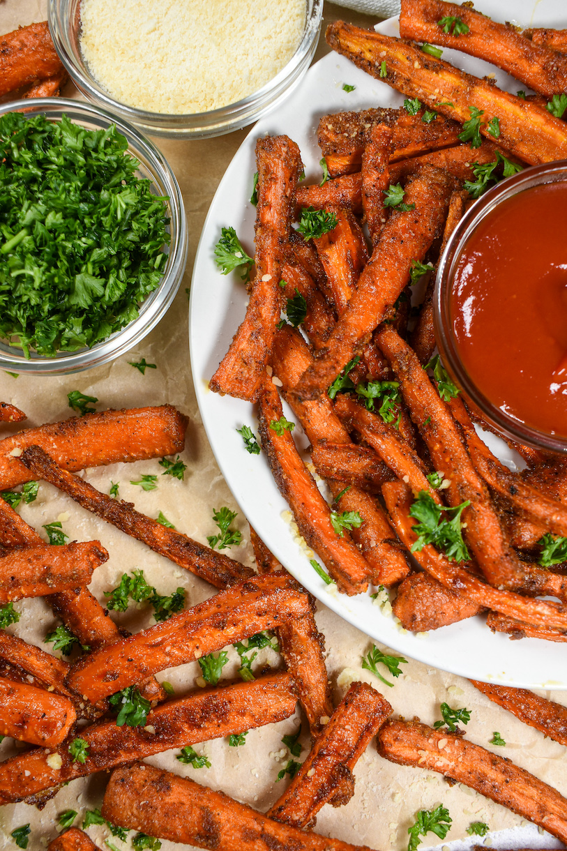 A plate of carrot fries with dishes of cheese, parsley, and ketchup