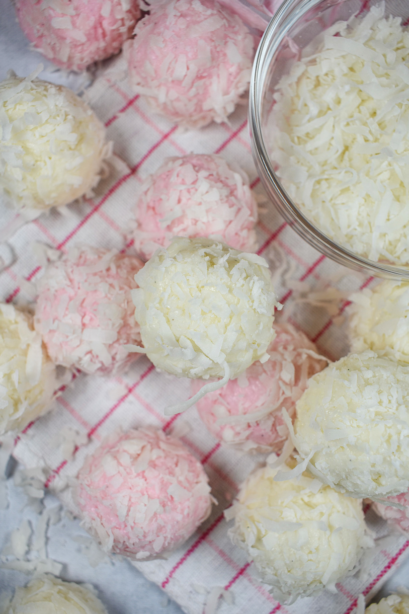 Coconut truffles arranged on a plaid towel with a dish of shredded coconut