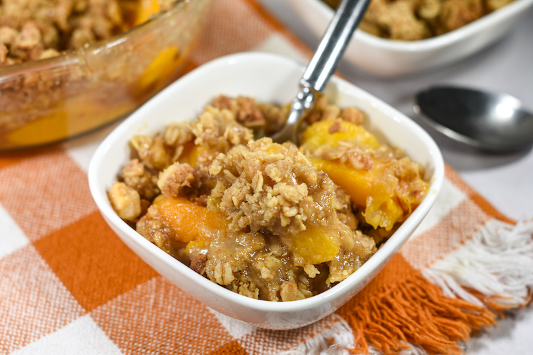 A small bowl of peach crisp with a spoon