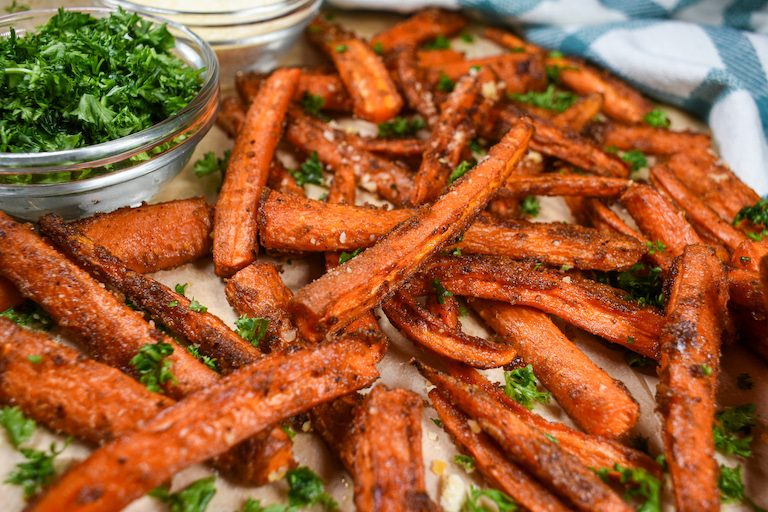 Carrot fries arranged on a sheet of parchment with a dish of chopped parsley