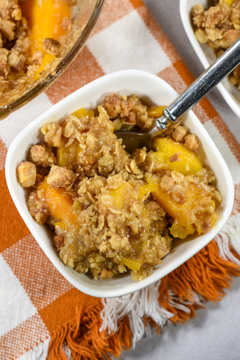 A small dish of peach crisp with a spoon