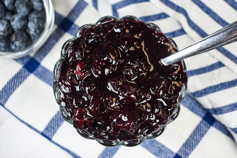 Looking down at a glass dish of blueberry compote arranged on a blue and white towel