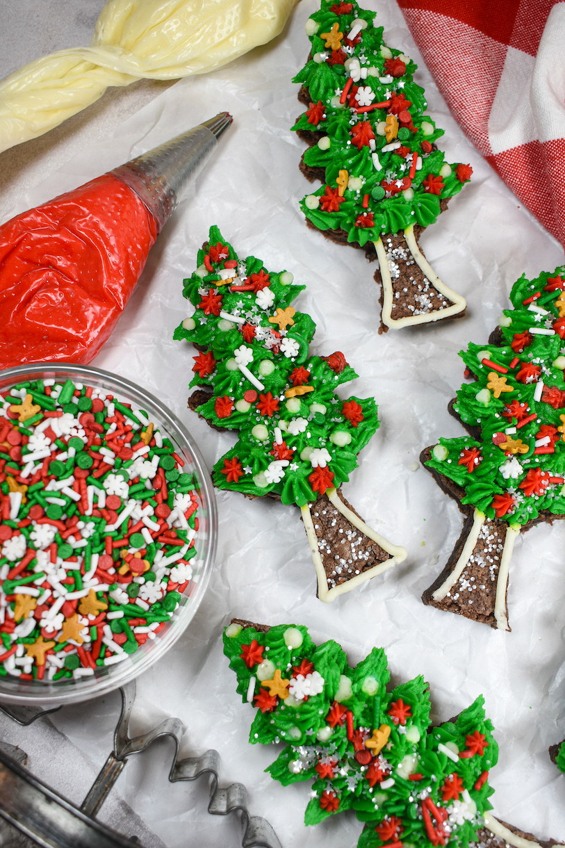 Horizontal shot of Christmas tree brownieson a white surface with piping bags and a dish of sprinkles
