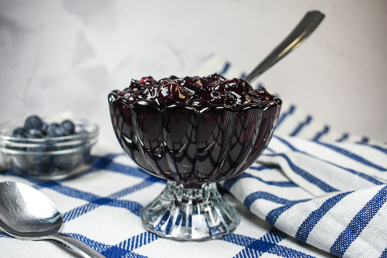A glass dish of blueberry compote with a spoon