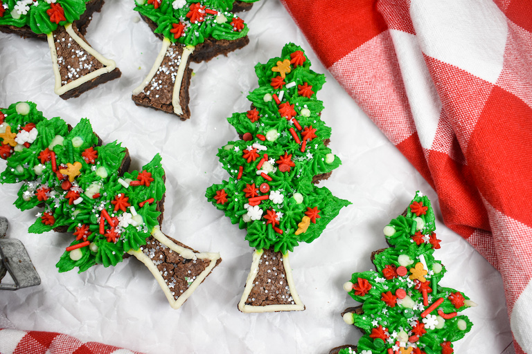 Christmas brownies shaped like trees, arranged on a white surface with a red checkered tea towel