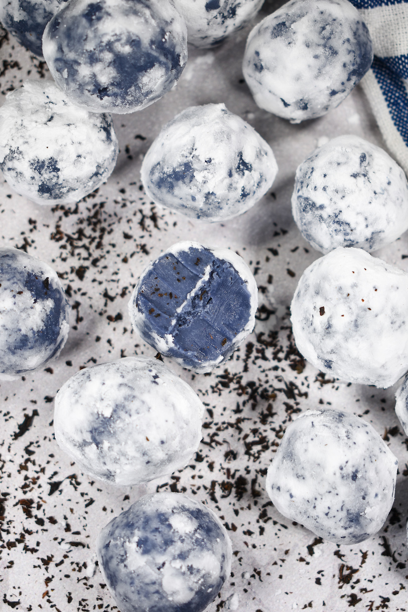 Earl Grey truffles ona white surface surrounded by bits of loose leaf Earl Grey tea