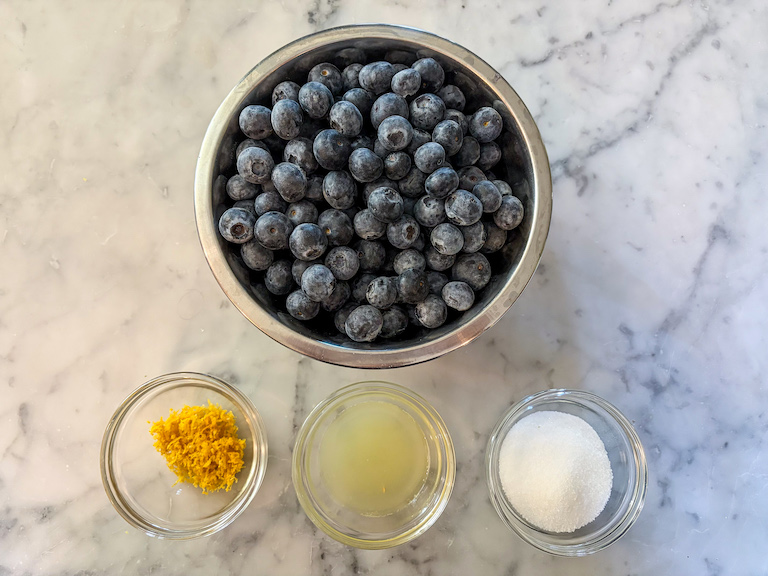 Blueberry compote recipe ingredients arranged on a marble surface