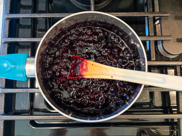 Blueberry compote in a pan on the stovetop with a spoon