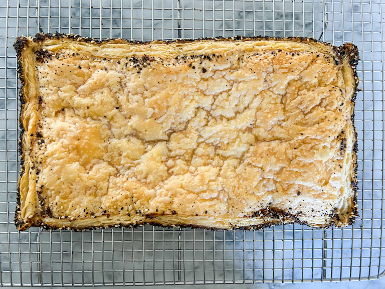A rectangle of everything bagel puff pastry cooling on a wire rack