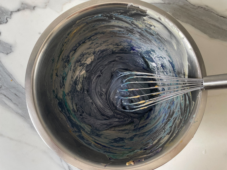A bowl of blue-tinted Earl Grey ganache with a whisk