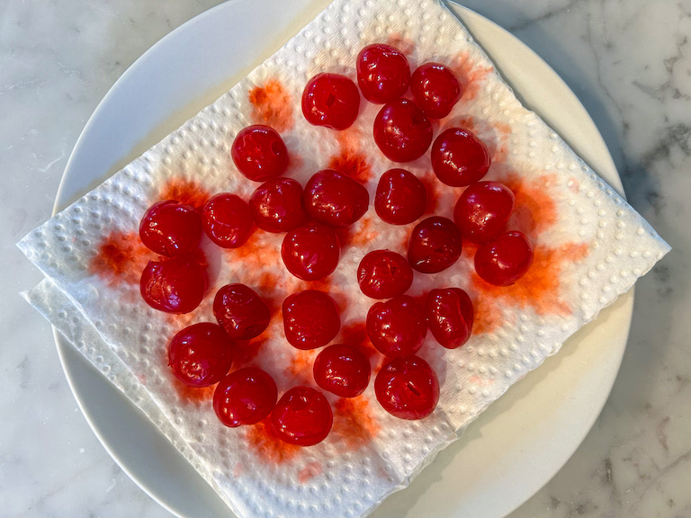 Maraschino cherries draining on a paper towel lined plate