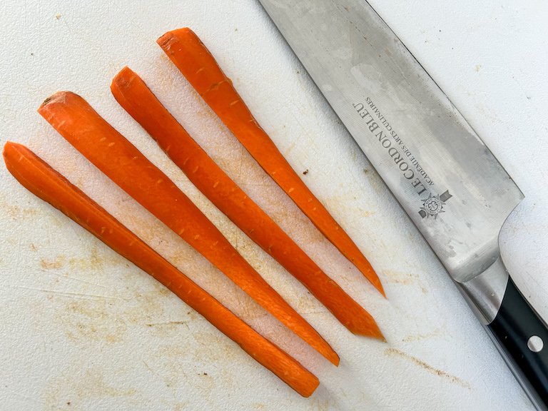 A knife on a cutting board with carrot sticks