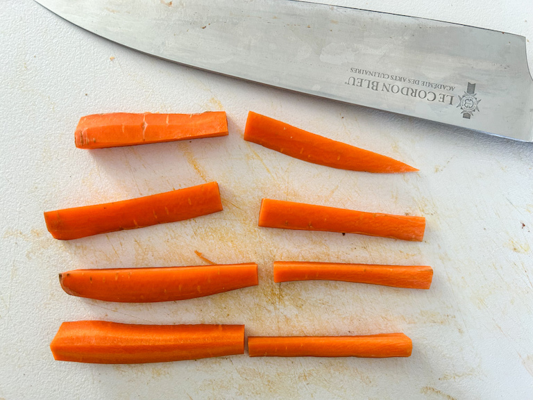 A knife on a cutting board with carrot sticks