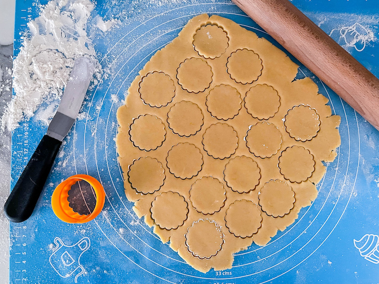 A roling pin, sheet of dough, cutter, and palette knife on a floured mat