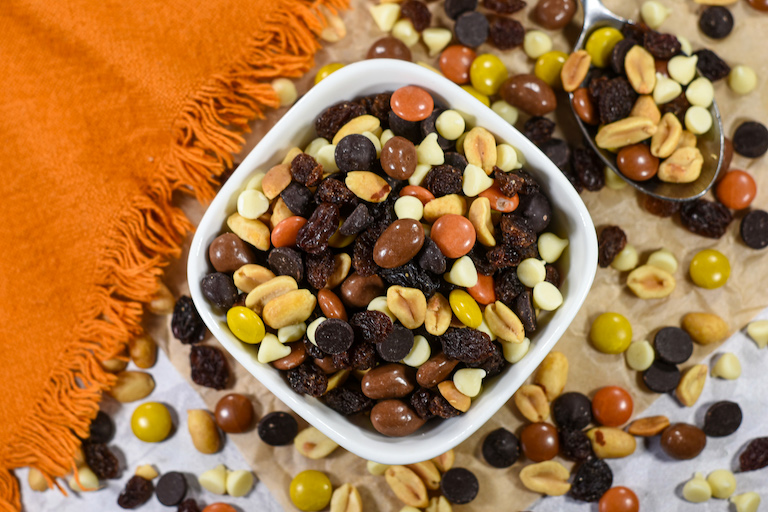 A dish of peanut butter chocolate trail mix on a sheet of parchment with an orange tea towel