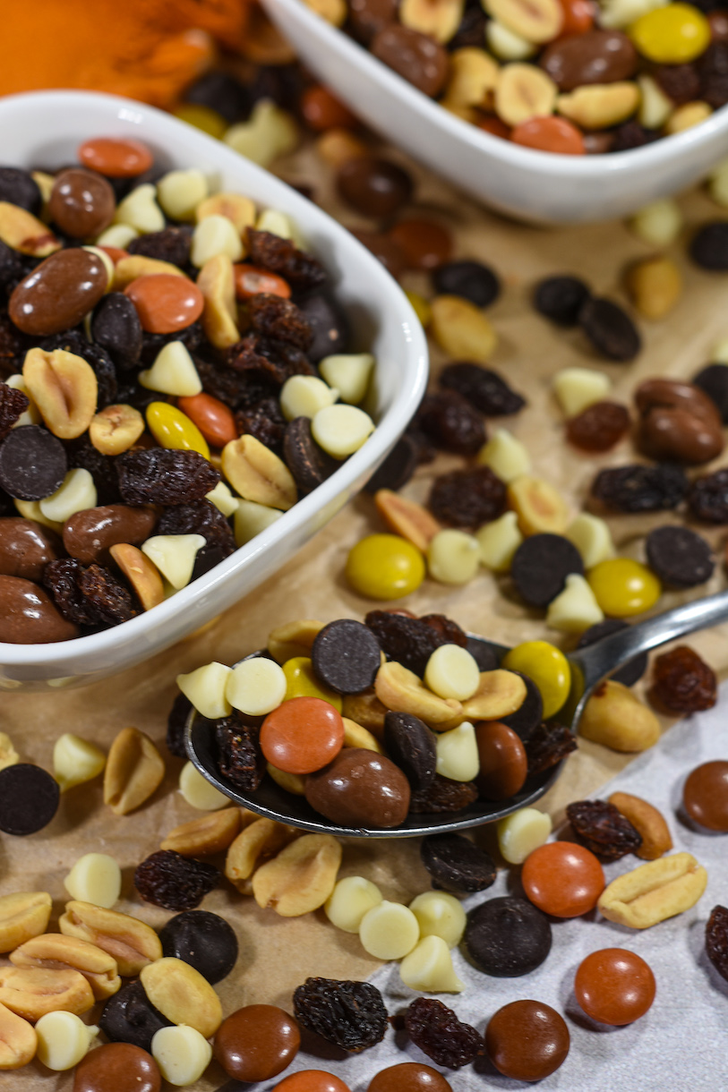 A spoonful of trail mix surrounded by peanuts, Reese's Pieces, and chocolate chips