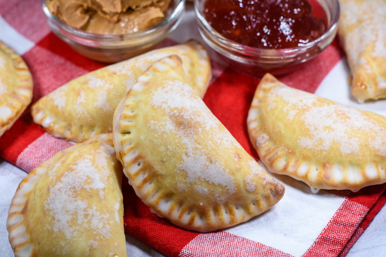 Peanut butter and jelly hand pies arranged on a red and white plaid towel