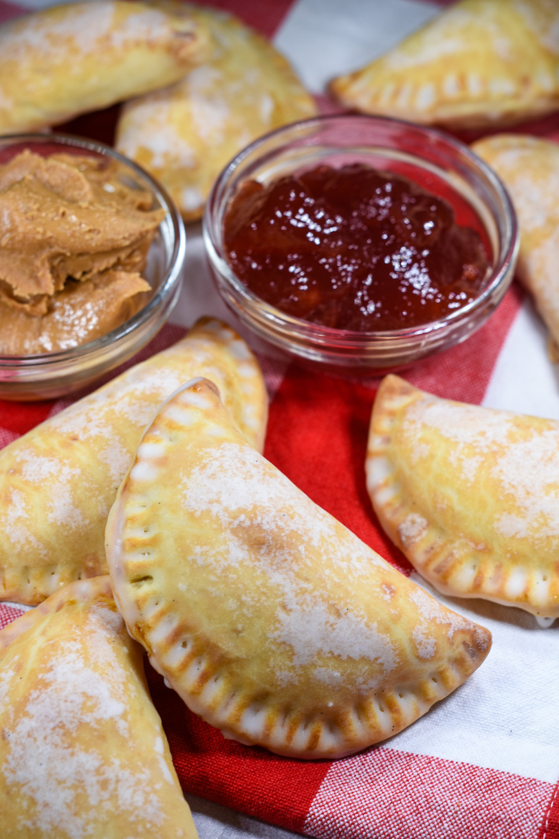 Dishes of peanut butter and jelly on a plaid tea towel with pb&j hand pies