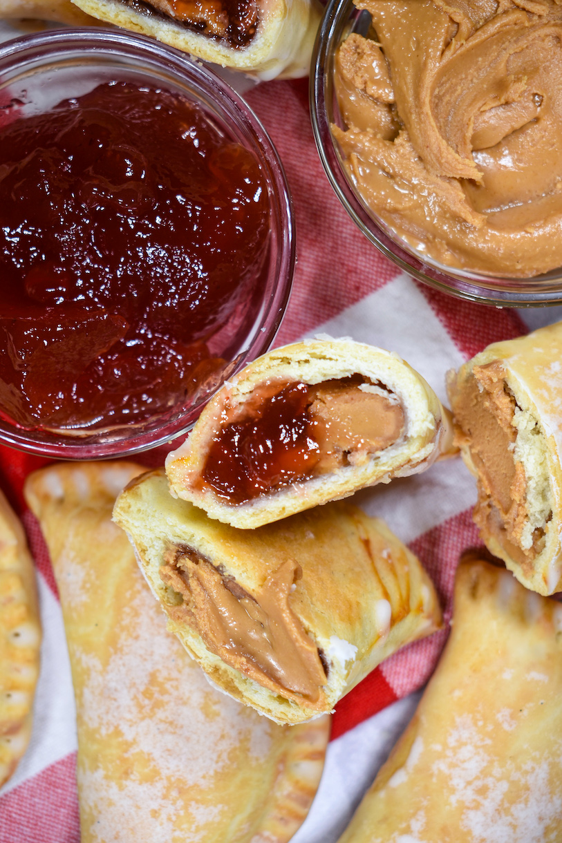 Peanut butter and jelly hand pies on a tea towel with dishes of peanut butter and jelly