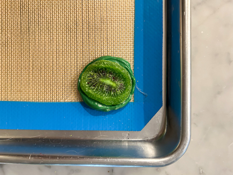 A dried kiwi pressed on top of melted green chocolate