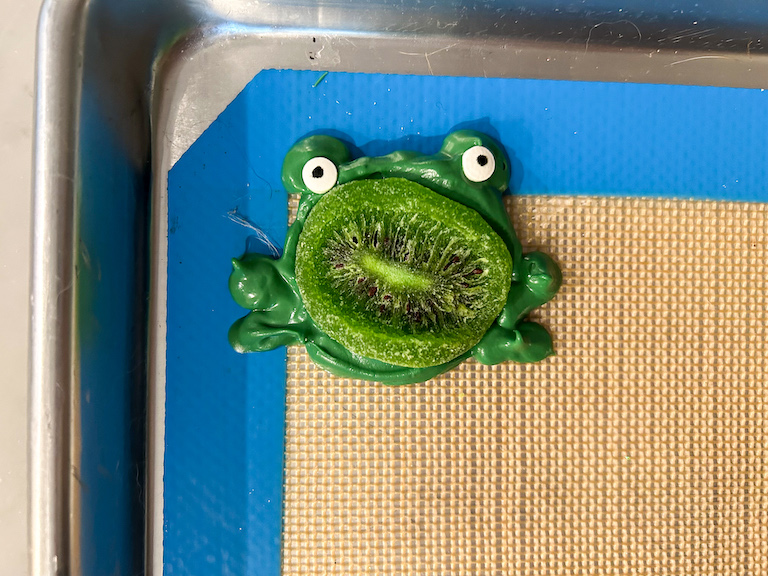 A chocolate frog with kiwi and candy eyeballs