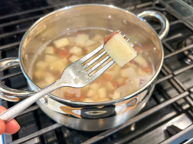 Fork testing the tenderness of a boiled red potato
