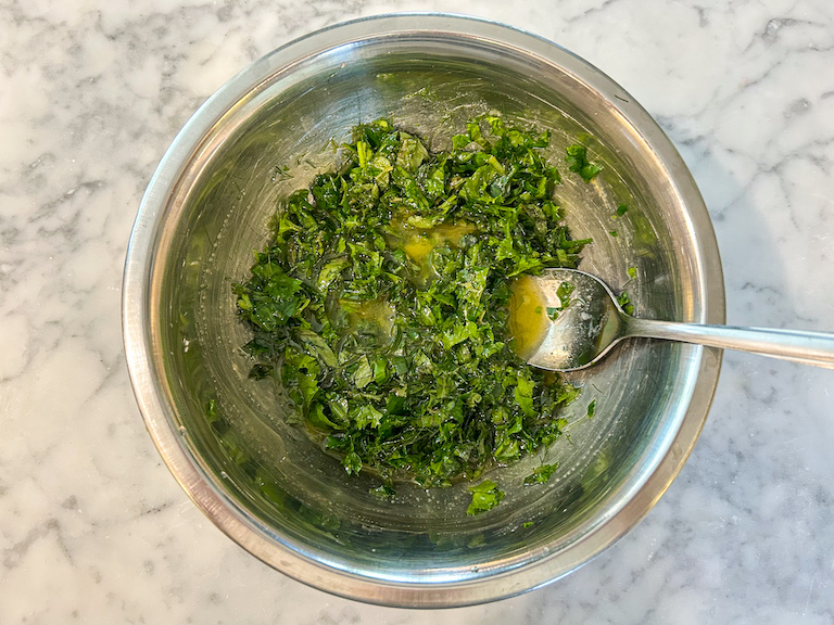 Olive oil and chopped green herbs in a bowl with a spoon