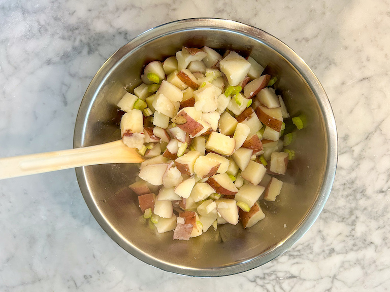 Spoon stirring together red potatoes and chopped celery in a bowl