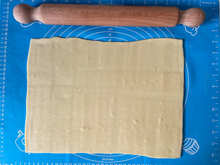 A sheet of pastry and a rolling pin on a rolling mat