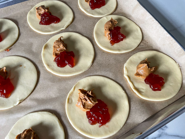 Spoonfuls of jelly and peanut butter on discs of unbaked shortcrust pastry