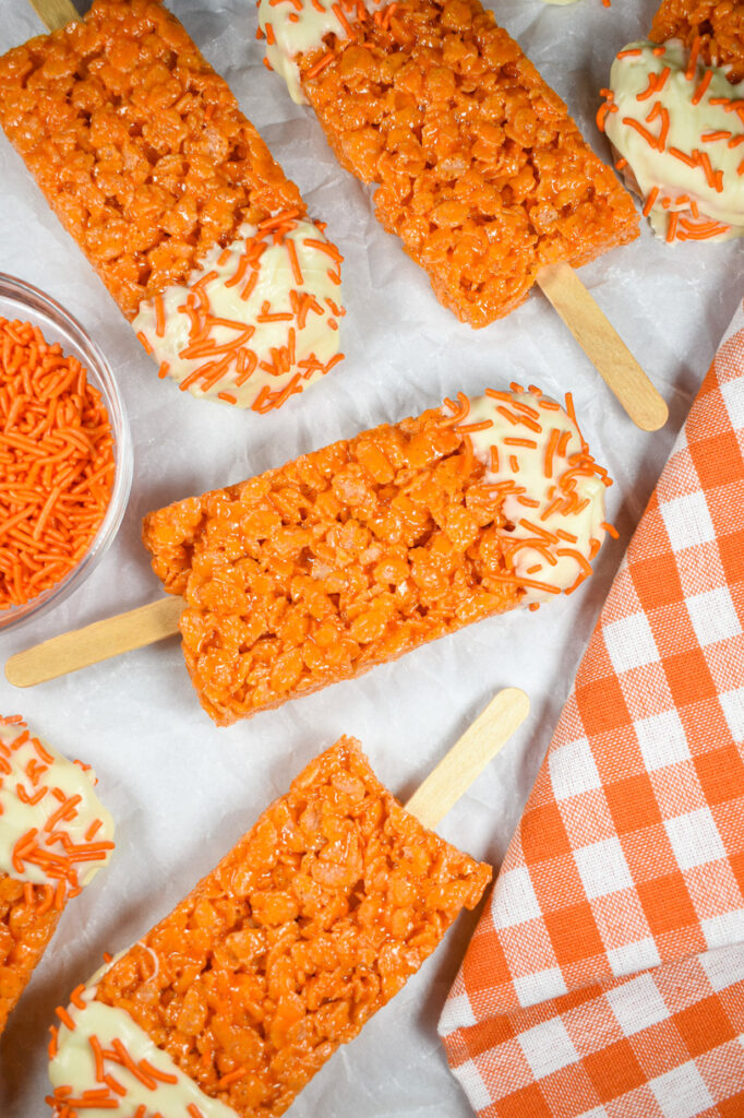 Creamsicle pops arranged on a white surface with a dish of sprinkles and checkered orange towel