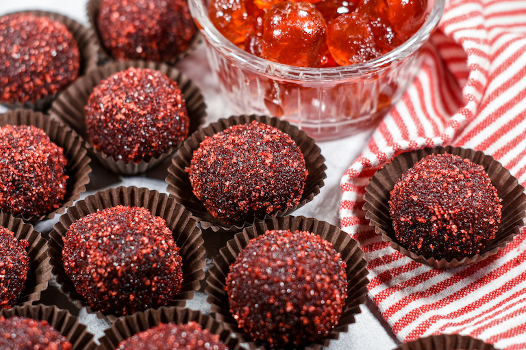 Chocolate truffles in truffle cups, arranged on a red and white striped towel with a dish of cherries