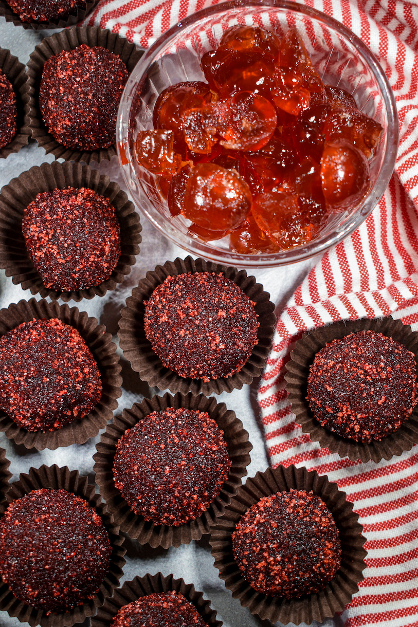 Chocolate cherry cola truffles on a white surface with a striped towel and dish of glace cherries