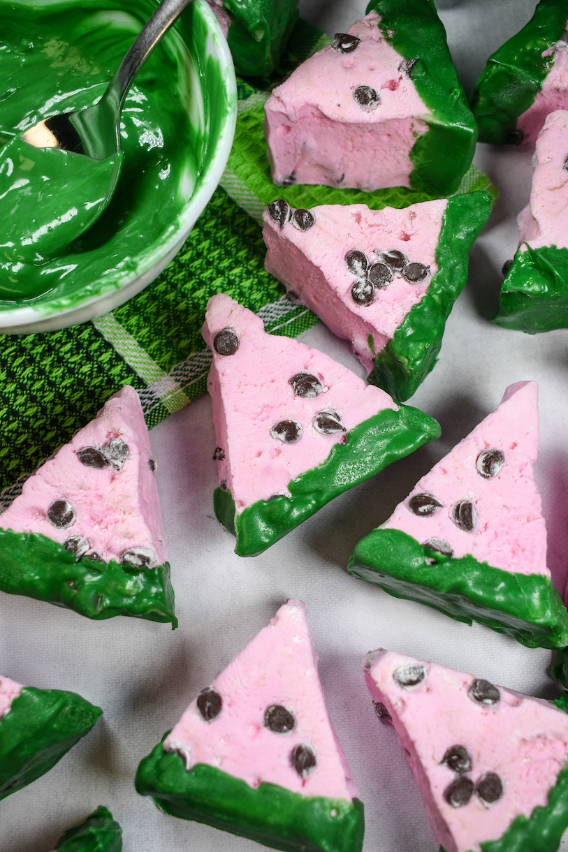 Pink watermelon marshmallows arranged on a green towel with a dish of green chocolate