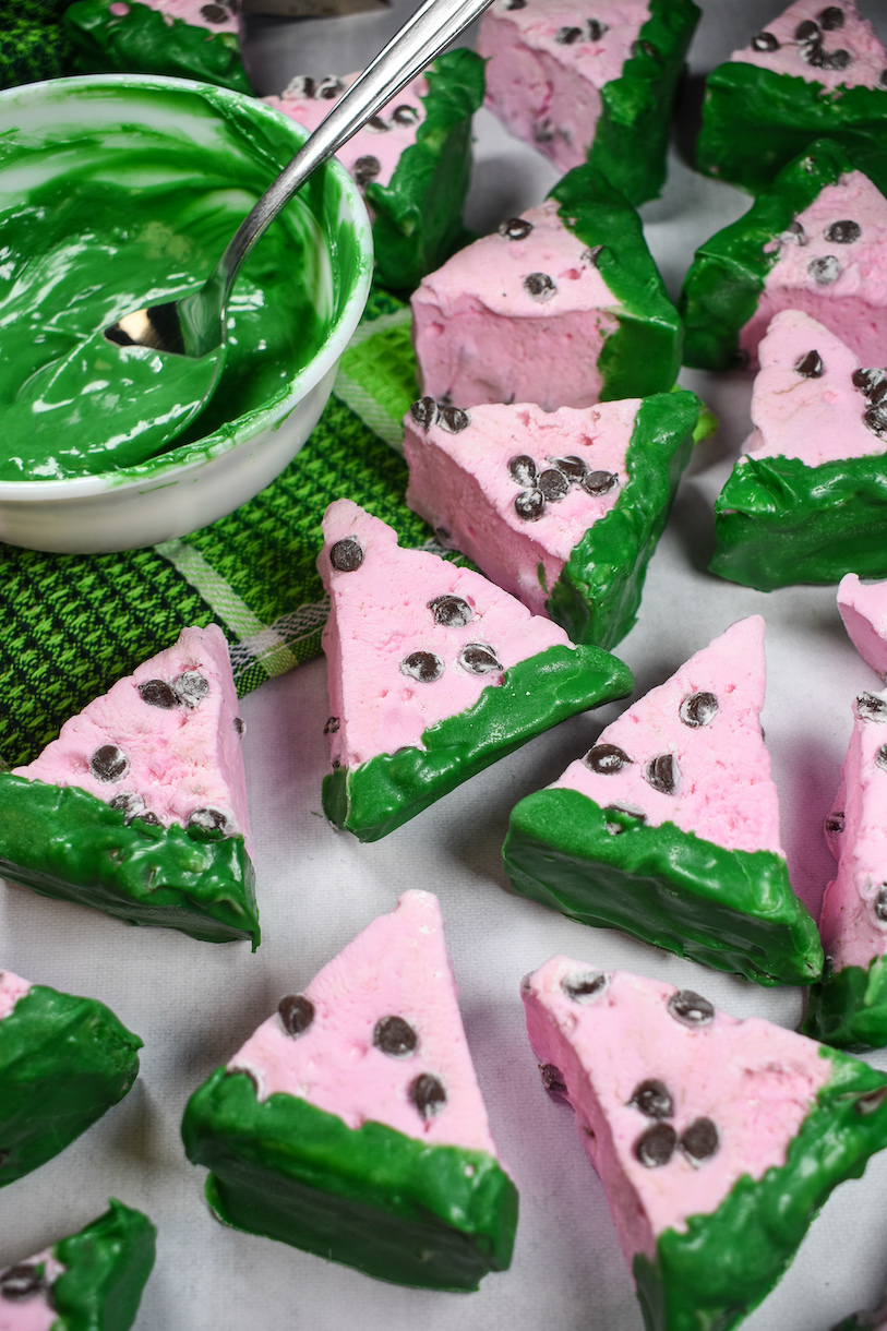watermelon marshmallows on a white surface with a dish of melted green chocolate
