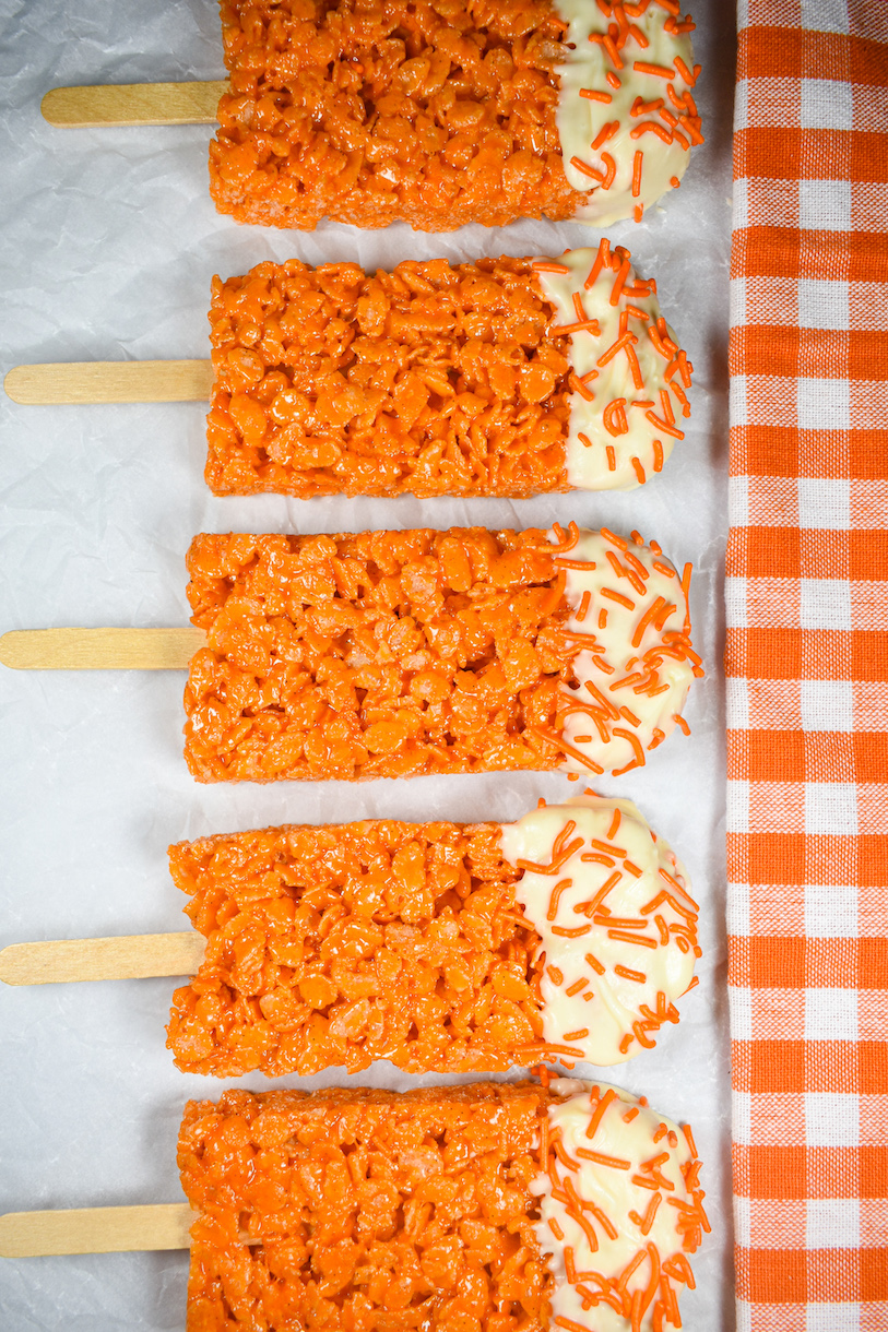 A row of Creamsicle cereal treats arranged vertically on a white surface next to an orange checkered tea towel