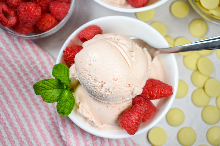 Looking down at a dish of raspberry ice cream garnished with mint leaves and fresh berries