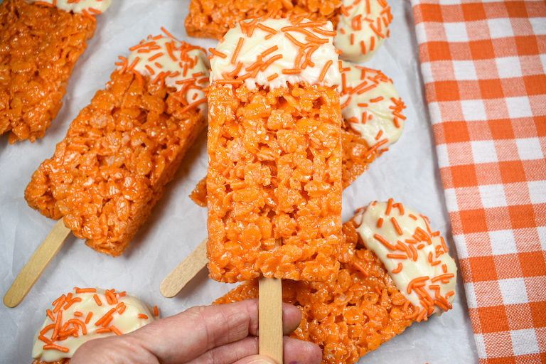 Hand holding a Creamsicle cereal treat popsicle decorated with white chocolate and orange sprinkles