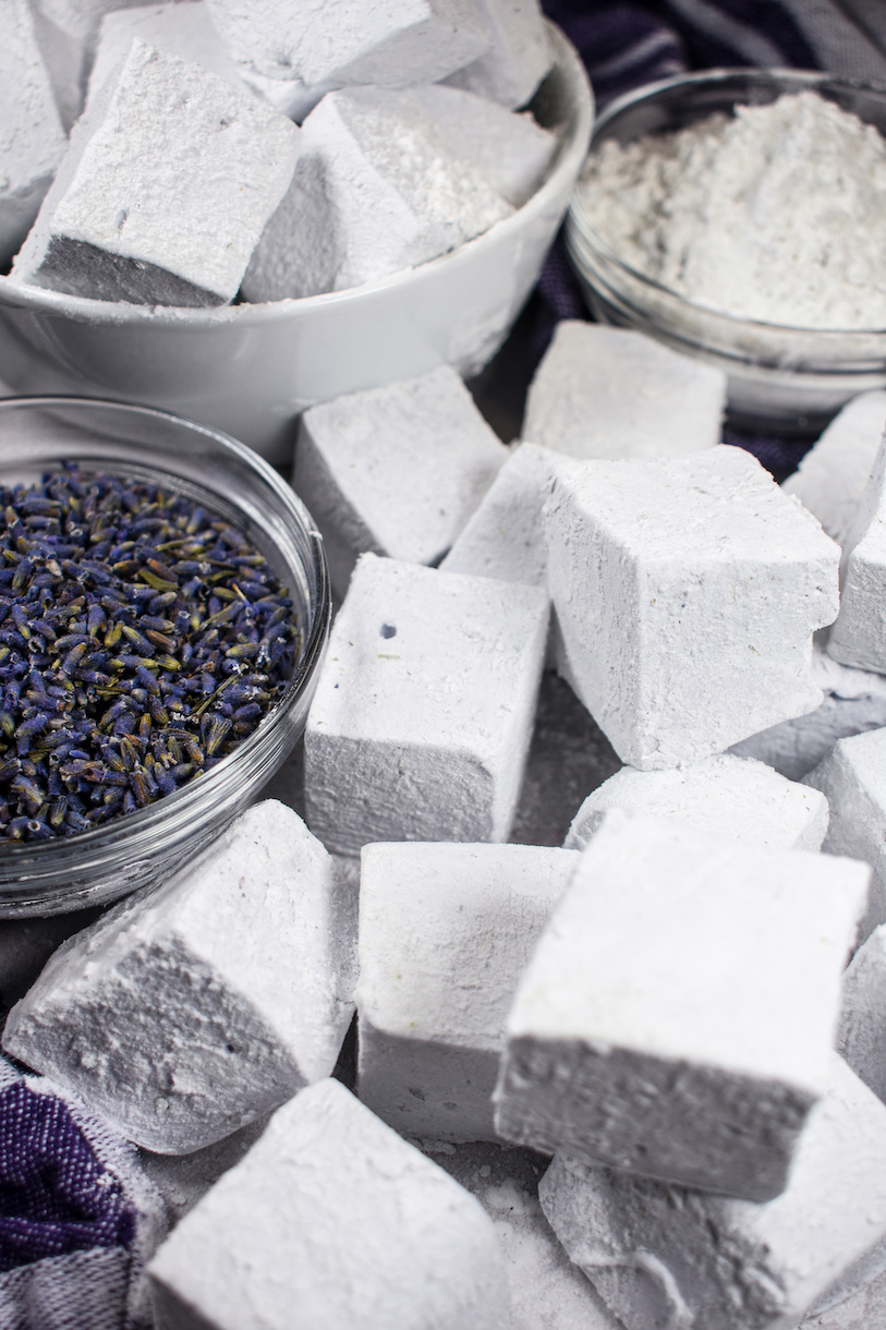 Lavender marshmallows on a white surface with a dish of dried lavender