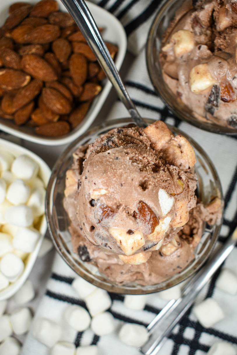 Looking down at a dish of rocky road ice cream surrounded by nuts and marshmallows