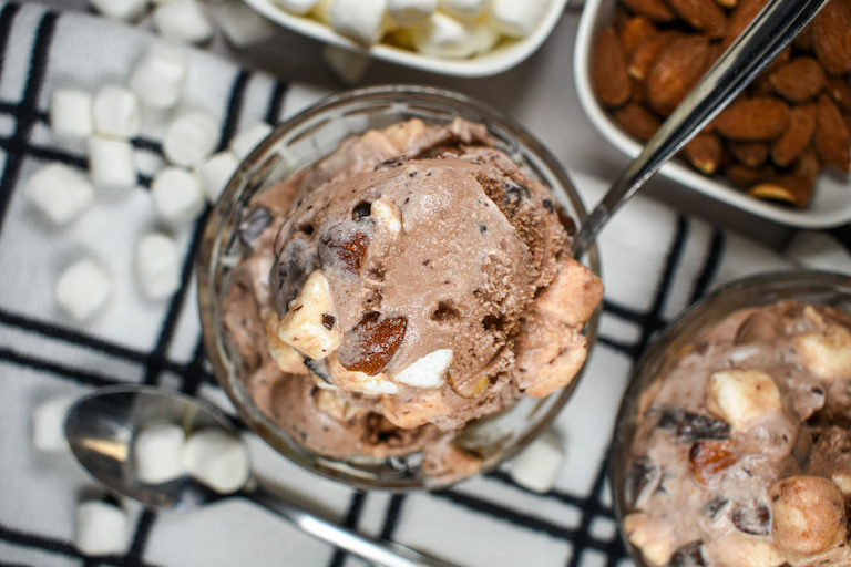 A dish of rocky road ice cream surrounded by almonds and mini marshmallows