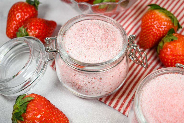 A jar of strawberry sugar surrounded by fresh strawberries
