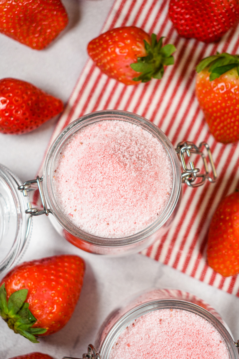 A jar of strawberry sugar on a striped towel, surrounded by fresh berries