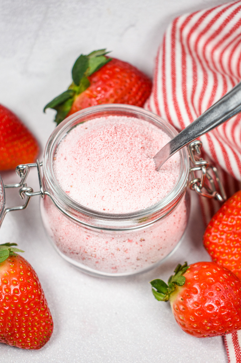 Fresh strawberries, a jar of homemade strawberry sugar, and a spoon
