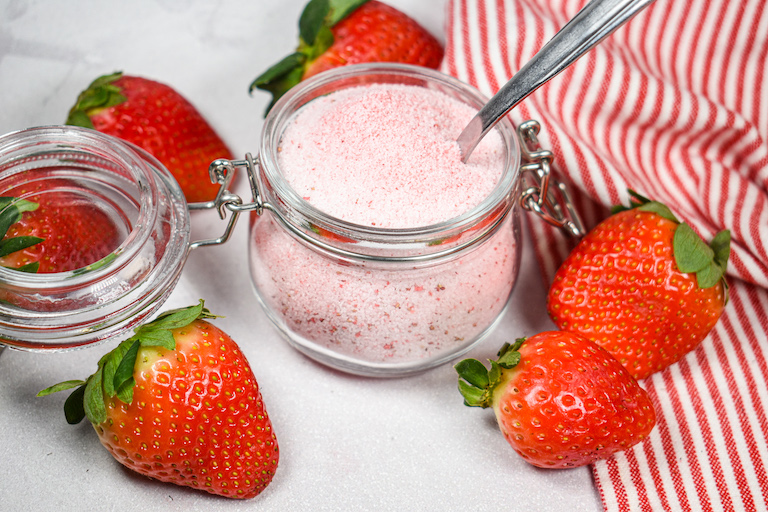 A glass jar of strawberry sugar surrounded by fresh strawberries