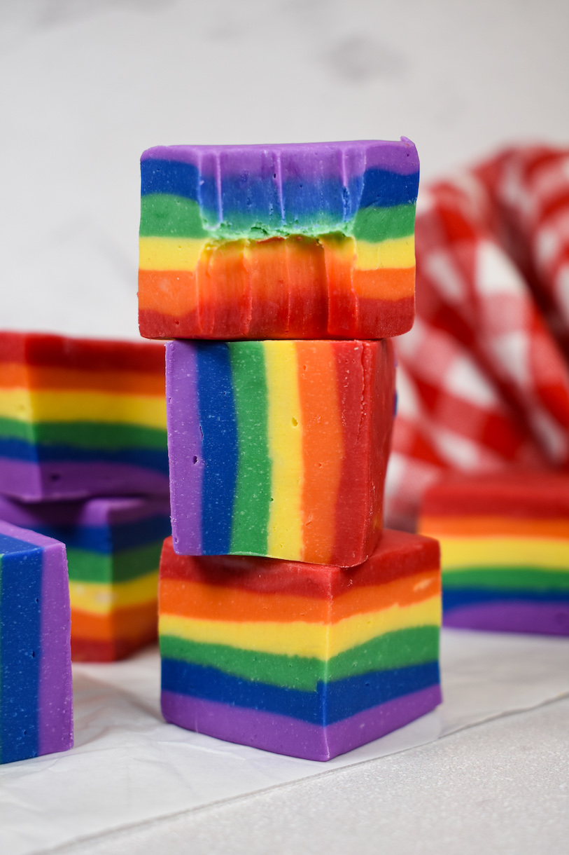 A stack of three pieces of rainbow fudge, with a bite missing from the top piece