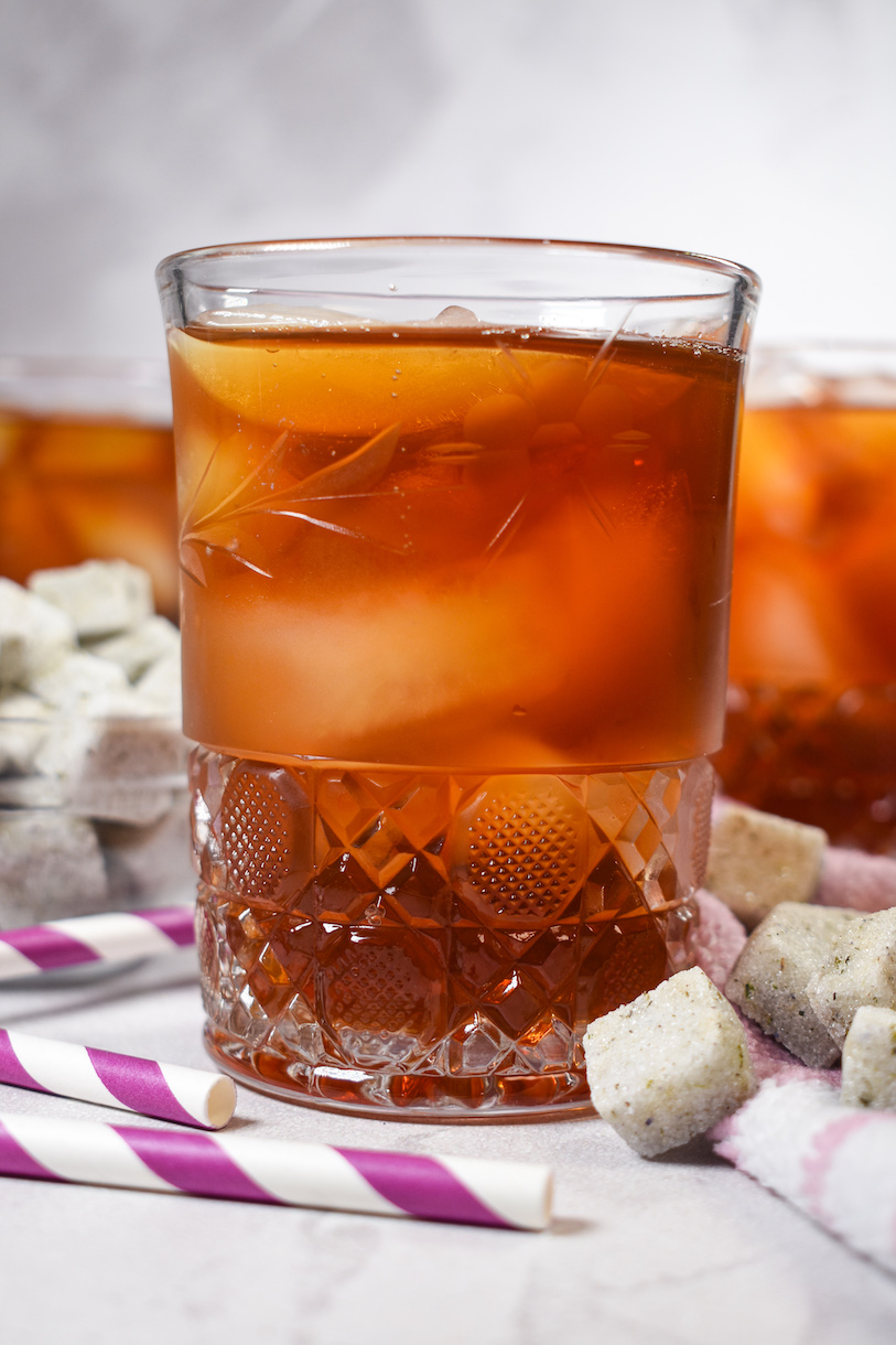A glass of iced tea on a white surface with sugar cubes and striped straws