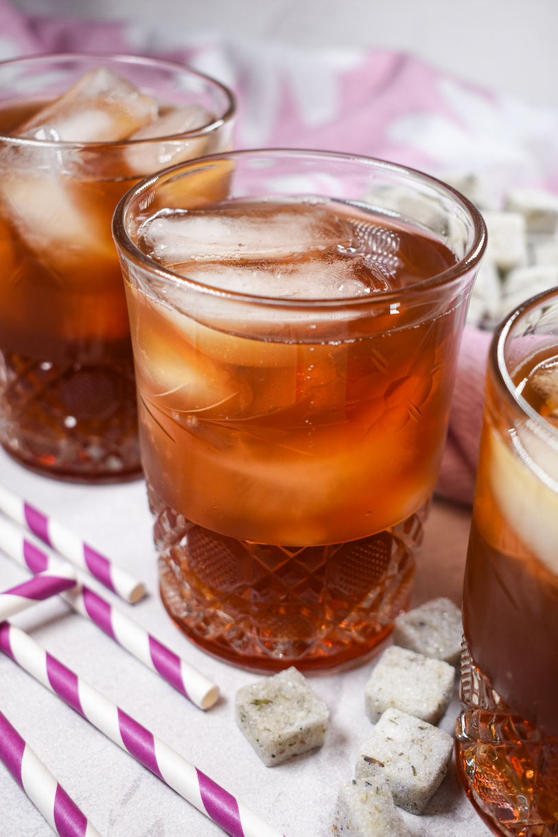 Three glasses of iced tea with lavender, along with striped straws and lavender sugar cubes